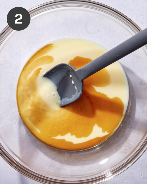 Condensed milk and vanilla in a glass bowl with a spoon.