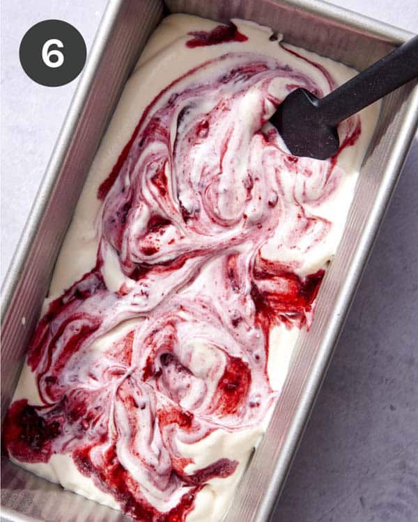No churn ice cream mixed with berries being layered in a loaf pan.