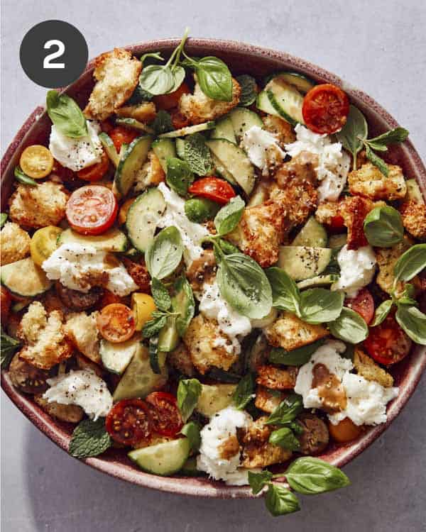 Panzanella salad in a bowl tossed with dressing and topped with herbs.