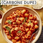 Spicy rigatoni in a bowl with some basil, red pepper flakes, and cheese on the side.