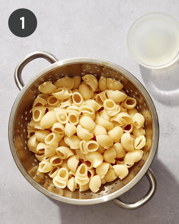 Cooked pasta in a colander with pasta water reserved on the side.