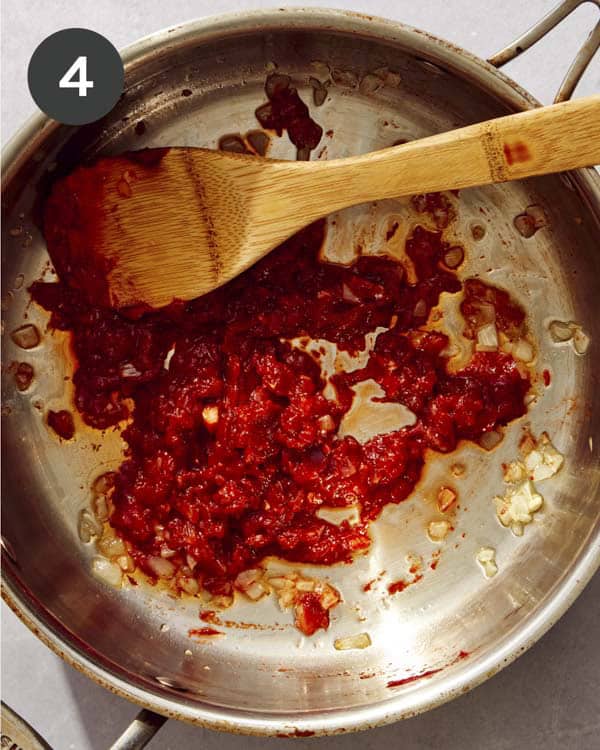 Tomato paste and garlic being cooked in a pan with a wooden spoon in it.