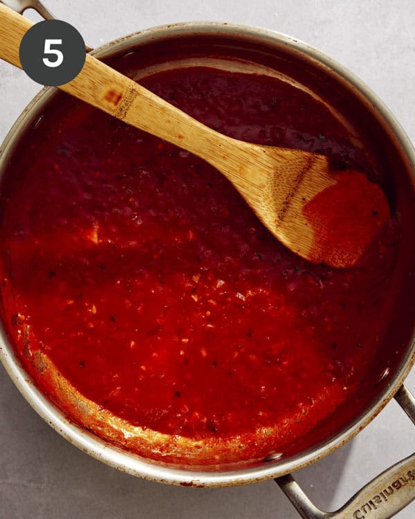 Tomato sauce being simmered in a pan with a wooden spoon.