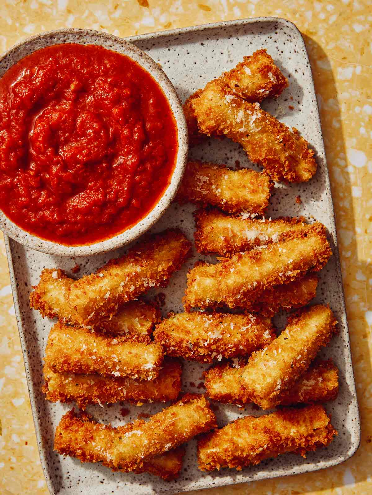 Close up on a platter of fried zucchini with marinara sauce next to it.