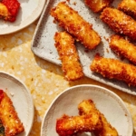Fried zucchini on a platter with some plates next to it.