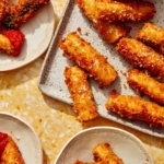 Fried zucchini on a platter with some plates next to it.