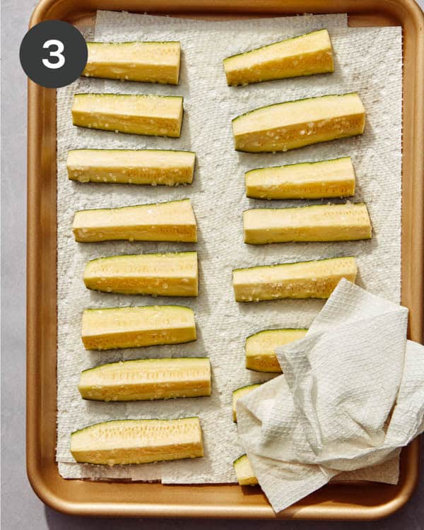 Zucchini wedges with salt being wiped off with a paper towel.
