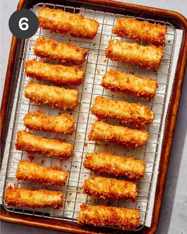Freshly fried zucchini wedges on a wire rack with salt on them.