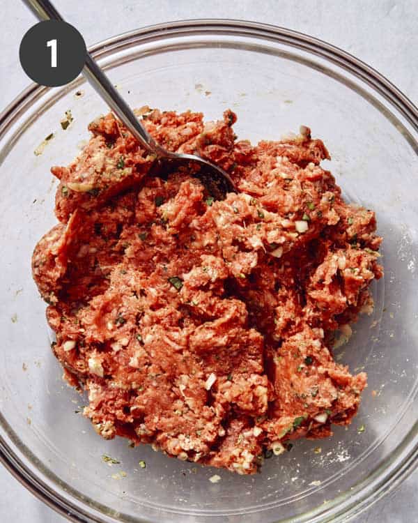 A glass bowl full of ground beef with seasonings being mixed in.