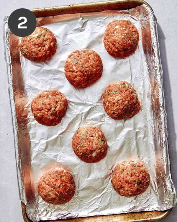 Ground beef formed into meatballs on a baking sheet.