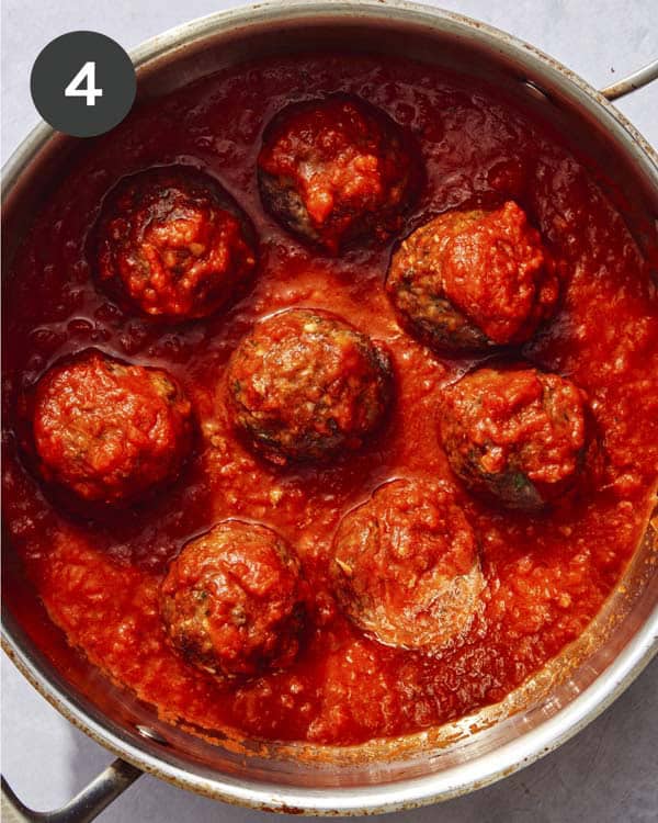 Meatballs cooking in a skillet with marinara sauce.