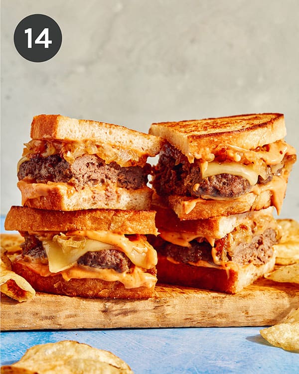 Two patty melts on a cutting board cut in half with chips on the side.