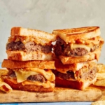 Two patty melts on a cutting board cut in half with chips on the side.