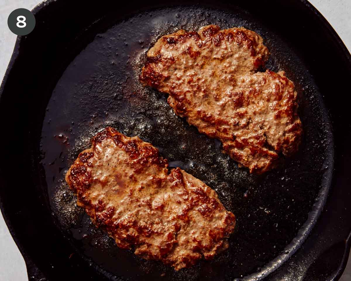 Ground beef patties being cooked in a cast iron skillet.