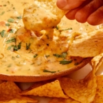 A hand dipping a chip in queso that is in a bowl.