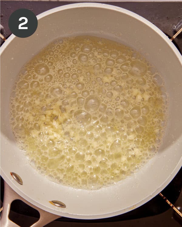 Butter melted in a skillet with garlic cooking in it.
