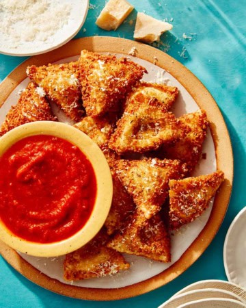 Toasted ravioli on a platter served with marinara sauce.