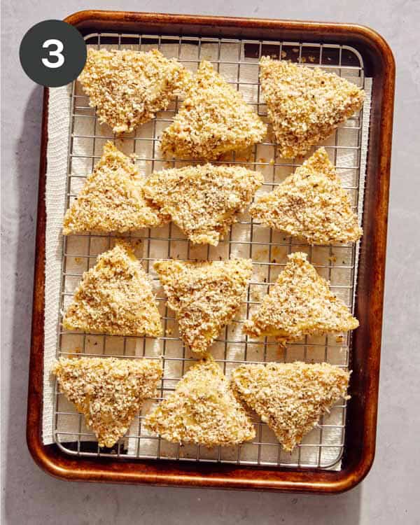 Ravioli coated in breadcrumbs on a baking sheet.