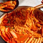 Budae Jjigae being served with chopsticks.