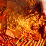 Budae Jjigae being served with chopsticks.