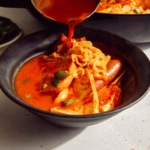 Korean army stew or Budae Jjigae being ladled into a bowl.