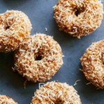 Baked pumpkin donuts on a surface with coconut.