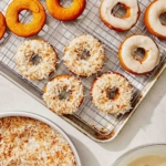 Baked pumpkin donuts being glazed and covered in coconut.