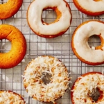 Baked pumpkin donuts being glazed and covered in coconut.