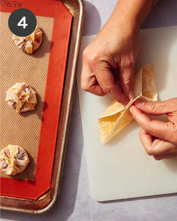 Hands folding phyllo dough over the top of brie cheese.