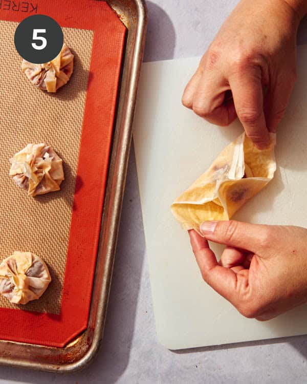 Hands folding phyllo dough over the top of brie cheese.