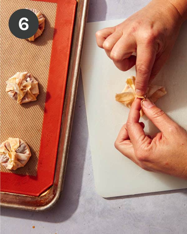 Hands folding phyllo dough over the top of brie cheese.