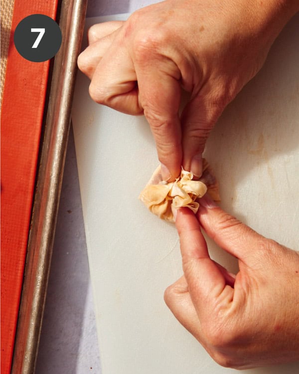 Hands folding phyllo dough over the top of brie cheese.