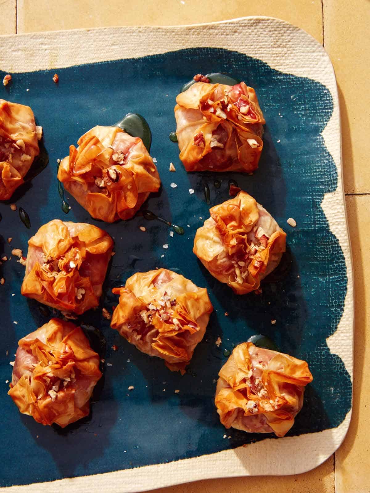 Crispy brie bites on a platter with honey and nuts.