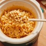 Mac and cheese in a crock pot with a spoon taking some out.