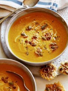 Creamy Pumpkin Soup recipe in a bowl with a spoon in it and parmesan crisps next to it, part of our Thanksgiving appetizers.