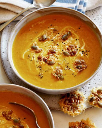Creamy Pumpkin Soup recipe in a bowl with a spoon in it and parmesan crisps next to it, part of our Thanksgiving appetizers.