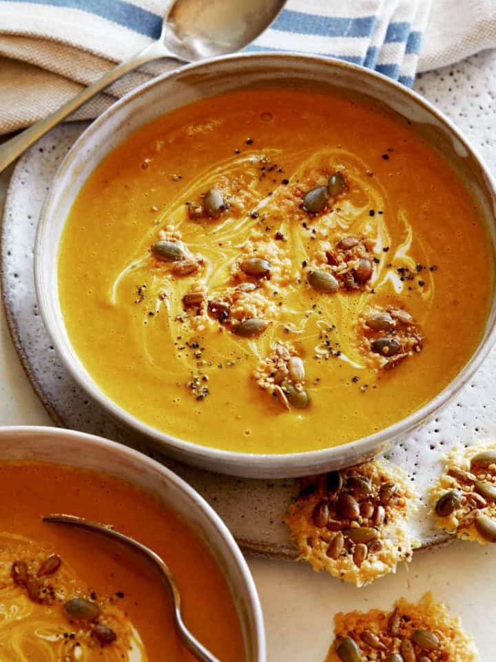 Creamy Pumpkin Soup recipe in a bowl with a spoon in it and parmesan crisps next to it, part of our Thanksgiving appetizers.