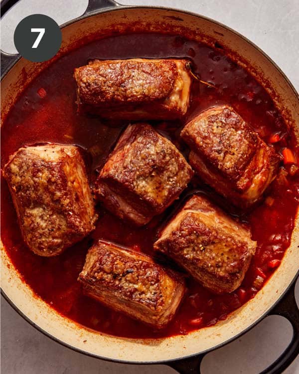Short ribs in a sauce in a skillet ready for the oven to braise.