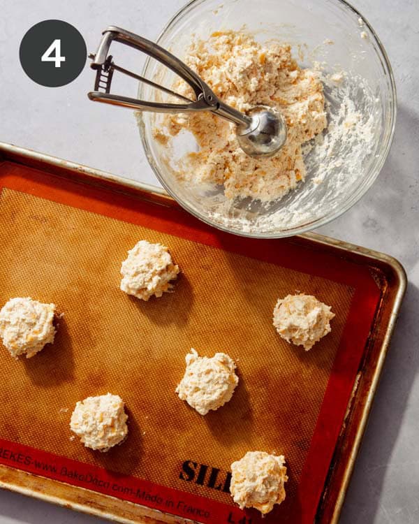 Cheddar bay biscuits being scooped onto a baking sheet.