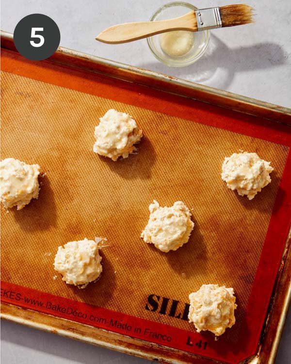 Raw biscuits being brushed with melted butter before baking.