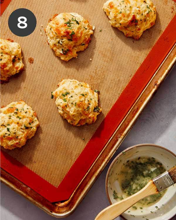 Cheddar bay biscuits being topped with a melted butter mixture.
