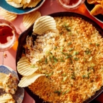 Jalapeño popper dip up close on the skillet with chips and drinks on the side.