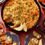 Jalapeño popper dip in a cast iron skillet with chips on the side and being dipped into it.