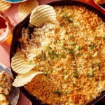 Jalapeño popper dip up close on the skillet with chips and drinks on the side.