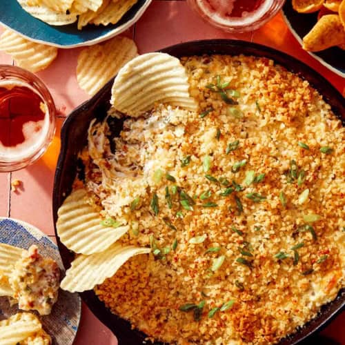 Jalapeño popper dip up close on the skillet with chips and drinks on the side.