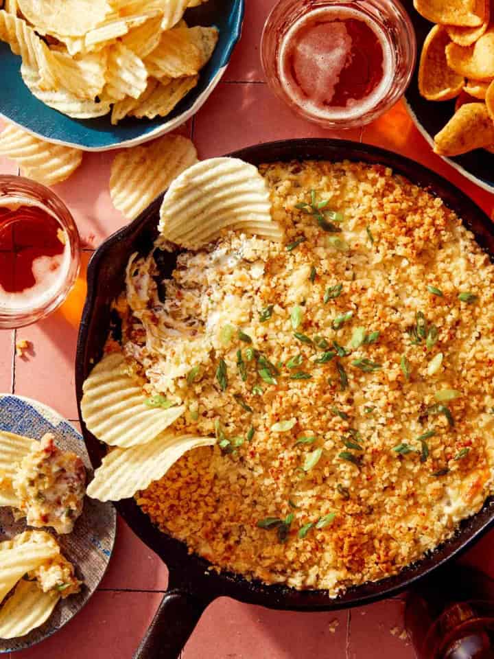 Jalapeño popper dip up close on the skillet with chips and drinks on the side.