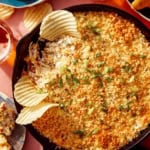 Jalapeño popper dip up close on the skillet with chips and drinks on the side.