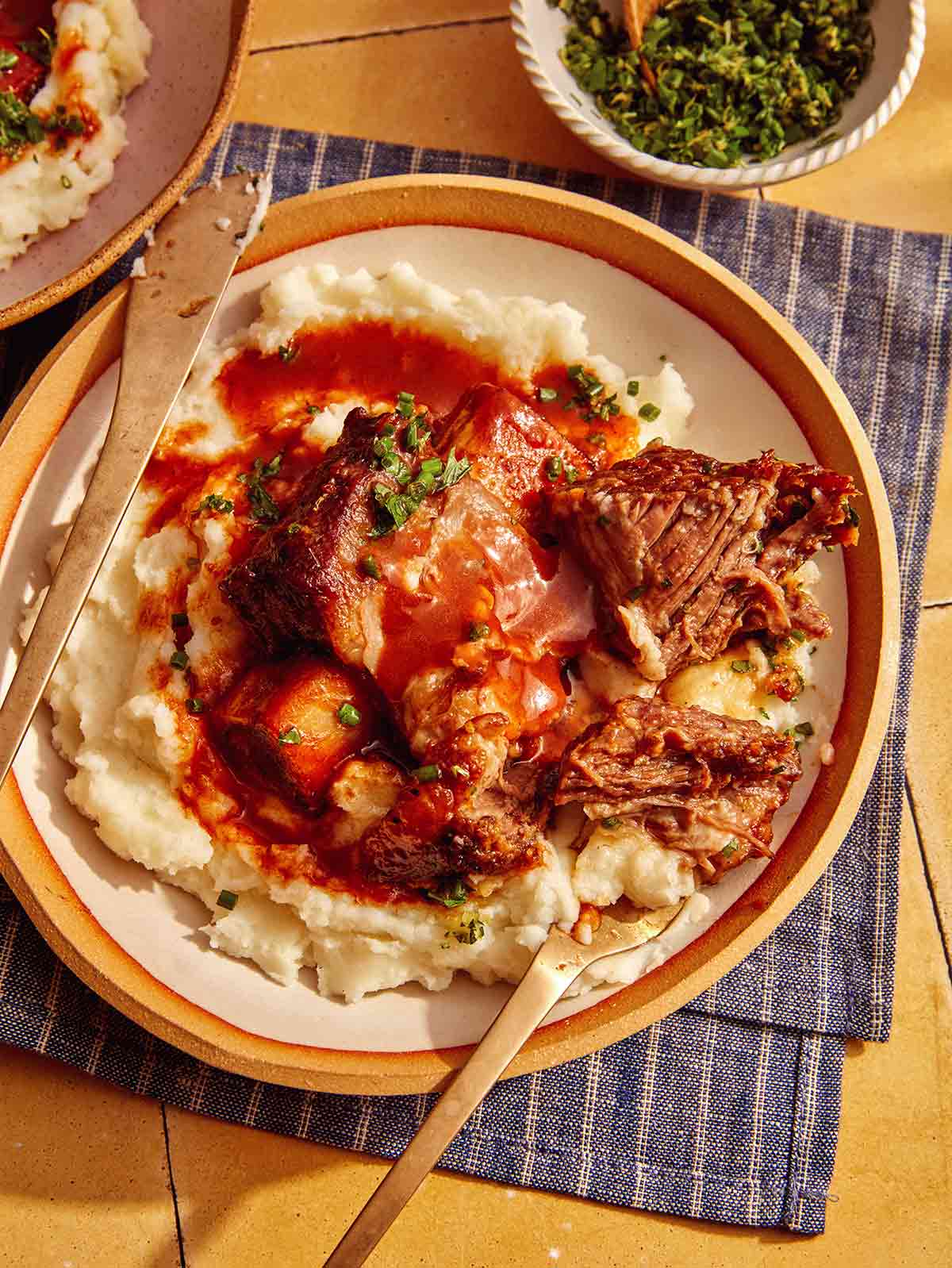 Braised short ribs on top of mashed potatoes in a bowl with a fork digging in.