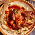 Braised short ribs on top of mashed potatoes in a bowl with a fork digging in.