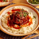 Braised short ribs on top of a bed of mashed potatoes in a bowl.